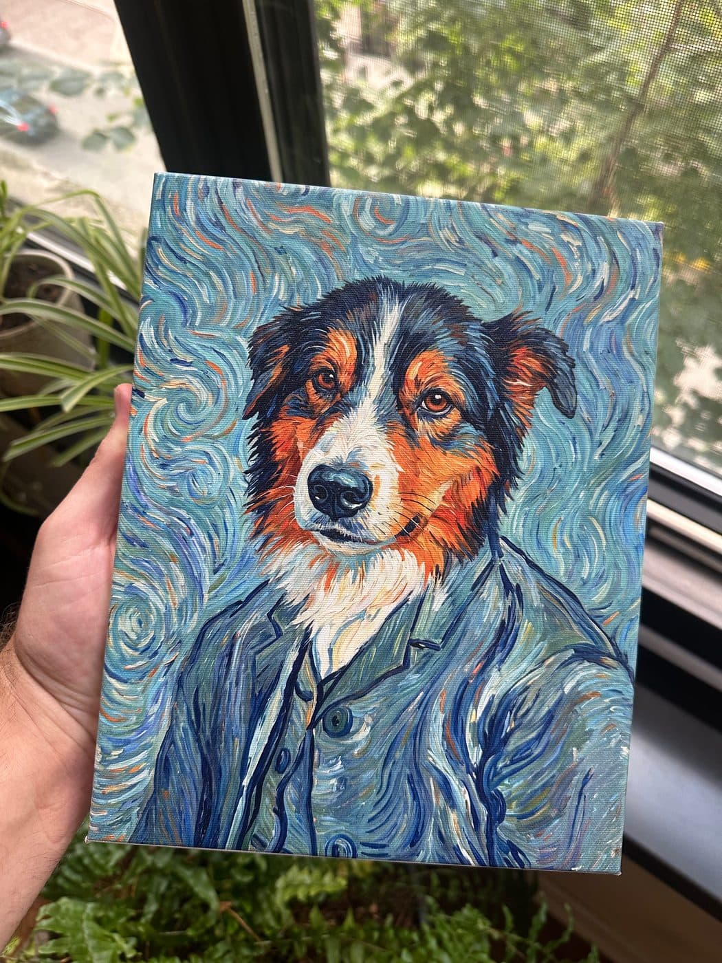 A hand holding the printed canvas of the Australian shepherd portrait beside a sunlit window.